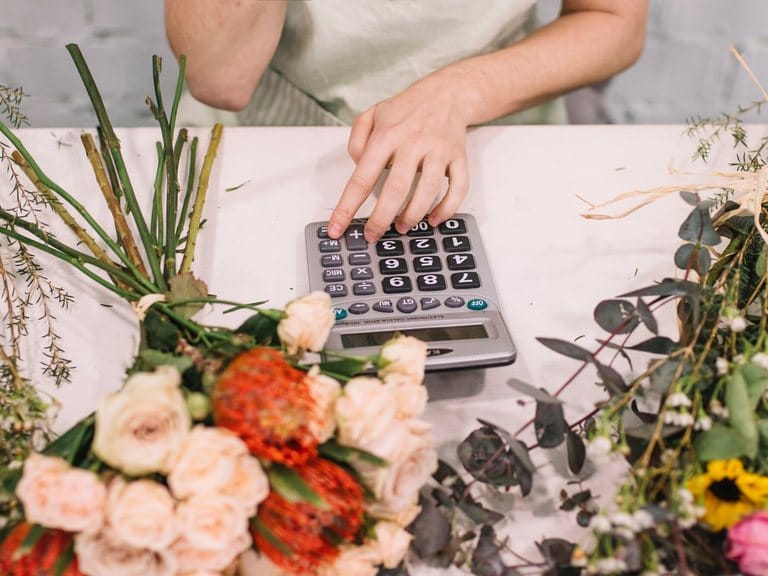 Florăreasă calculând prețul unui buchet, între flori proaspete